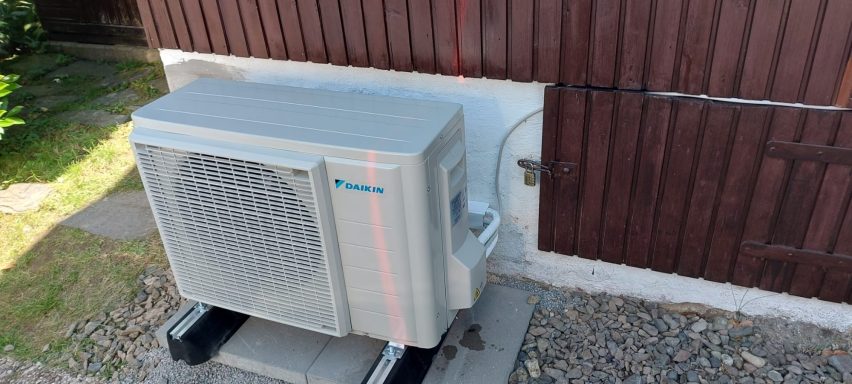 Klimaanlage auf einer Terrasse neben einer Wand mit Holzverkleidung.