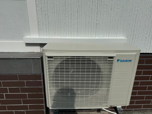 Klimaanlage an einer Wand montiert, mit sichtbarem Kühlergrill und Schatten.