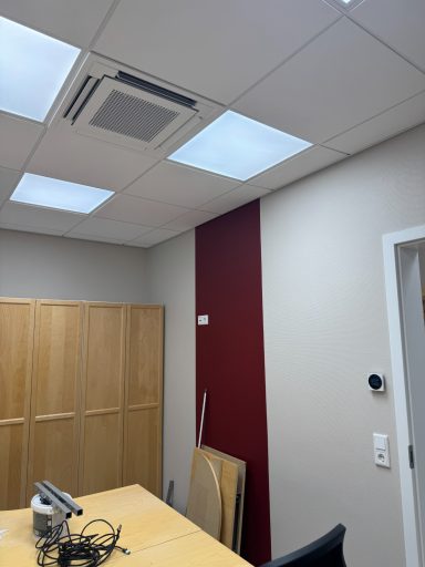Büro mit Holzschrank, roter Wand, Deckenbeleuchtung und Klimaanlage.